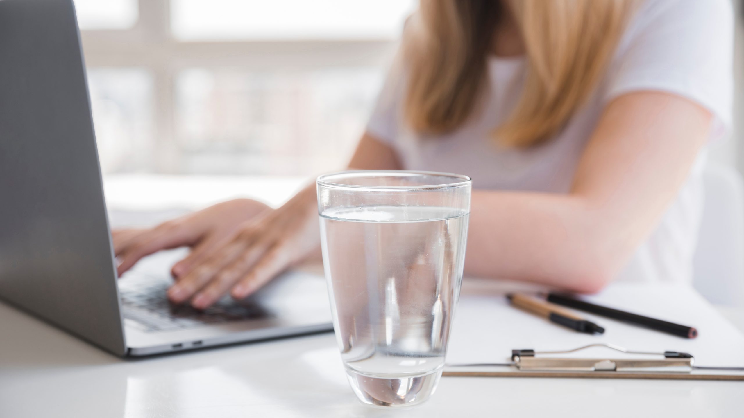 Mujer trabajando en el ordenador y un vasod e agua en primer plano